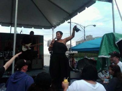 Keeshea Pratt on stage in an open air setting, singing to the onlookers.