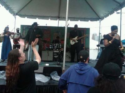 Keeshea Pratt on stage at an outdoor venue. She is singing as the people up front applaude.